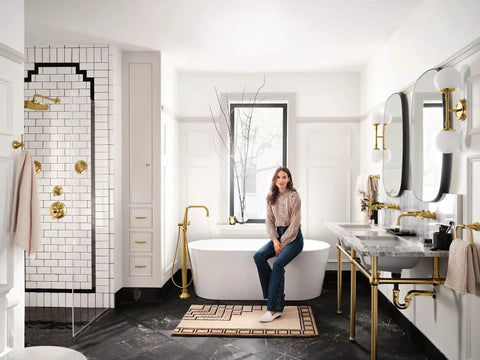 Bathroom with gold fixtures and a woman seated on a bathtub