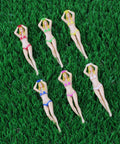 Six plastic figurines in colorful bikinis on grass, not related to Six Color 3 Inch Plastic Golf Tees Set Novelty Practice Tees.