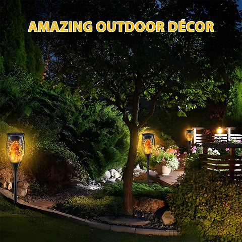 12 Pack Tiki Torch Lights With Flickering Flame Effect illuminating a garden pathway with greenery and flowers at night