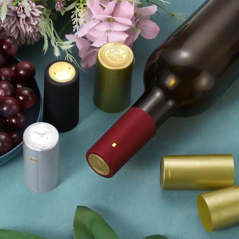 100 Pack Black PVC Heat Shrink Wine Bottle Caps 32mm Easy Seal Shrink Wrap Sleeves For DIY Wine Bottling And Beverages Keeps Flavor Fresh Leakproof Seal Wide Application Simple To Use displayed with wine bottle and grapes