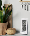 All In One Battery Operated Monochrome Digital Forecast Station With Wireless Display Time And Date Moon Phase Indoor And Outdoor Temperature Barometric Pressure Trend Arrows And Dynamic Weather Animations on a desk.