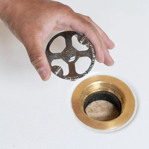 Hand holding No Calk Shower Drain Wrench with brass and plastic construction showing stainless steel core for easy removal