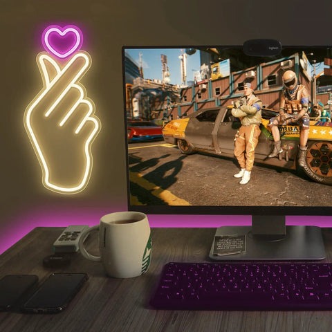 Finger Heart Neon Sign In Pink And Warm White For Bedroom And Game Room LED Light Hand Gesture Decor For K Drama And K Pop Fans Wall Decor Gift For Fans Vibe on a wall near a gaming setup, showing the hand gesture glowing brightly.