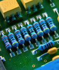 Close-up of blue axial metal-film resistors with color bands mounted on a green PCB