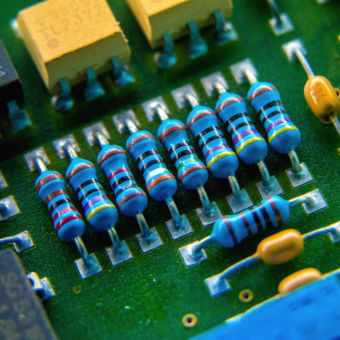 Close-up of blue axial metal-film resistors with color bands mounted on a green PCB
