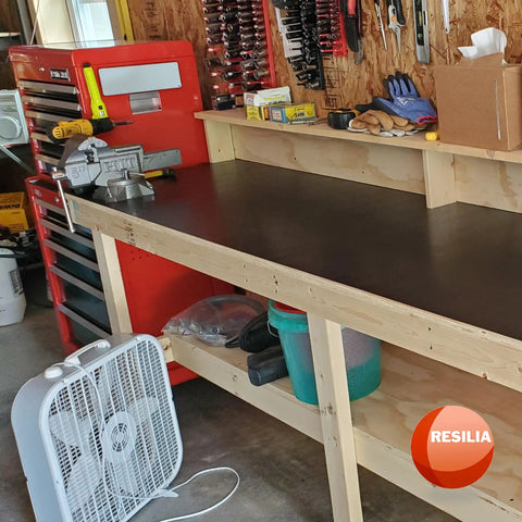 Heavy Duty 15 X 36 Inch Work Bench Mat With Scratch-Resistant 0.06 Inch PVC Protects Your Workbench, Table, And Tool Station From Painting, Woodworking, Crafting, And Building Messes Black Made In USA on a wooden workbench in a garage setting.