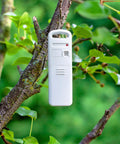Portable white weather sensor on a tree branch, with buttons and indicators, used for Weather Forecaster Alarm Clock With Wireless Qi Charging Pad Real Time Indoor And Outdoor Temperature And Humidity Calendar Illuminated LCD Display No Wires Needed.