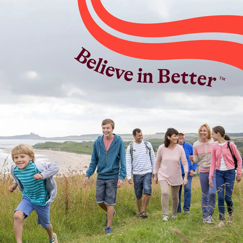 Group of people walking on a grassy path by the beach under a cloudy sky with 'Believe in Better' text in the sky