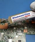Hand holding 10g syringe of High Active Soldering Flux For Electronics And PCBs, tacky paste for oxidized copper repair on circuit board.