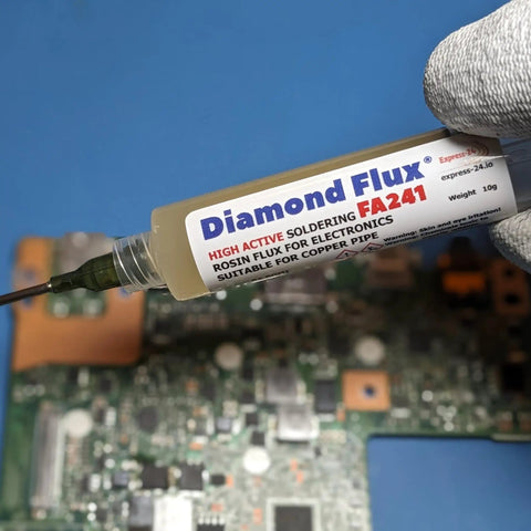 Hand holding 10g syringe of High Active Soldering Flux For Electronics And PCBs, tacky paste for oxidized copper repair on circuit board.