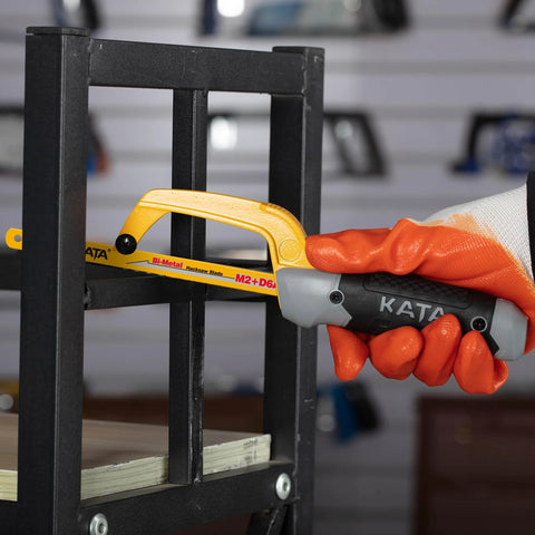 KATA mini hacksaw cutting a metal frame; yellow blade, aluminum frame, orange-gloved hand