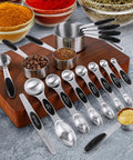 16 Piece Measuring Cups And Magnetic Spoons Set In Stainless Steel With 8 Nesting Cups And 7 Double Sided Magnetic Measuring Spoons Plus A Leveler For Dry And Liquid Ingredients A Handy Kitchen Must Have displayed on a wooden board with spices and coffee beans.
