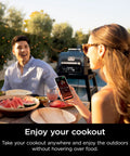 Couple enjoying a meal outdoors with Woodfire Pro Connect Deluxe XL Backyard Grill and Smoker With Bluetooth App Control in background.