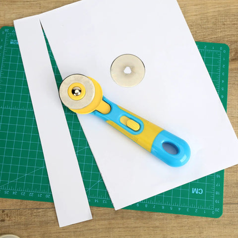 45mm Rotary Cutter Kit With One Extra Blade, Ergonomic Handle, A Real Workhorse With Ultra Sharp Steel Blades For Precise Fabric, Scrapbooking And Craft Cutting, Easy Grip, Smooth Cuts, Great For Quilting And DIY Projects. 45mm rotary cutter on paper and cutting mat