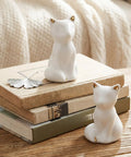 Level Up Your Bathroom Vibe With This Dope Set Of Ceramic Cat Toilet Bolt Covers And Floor Screw Caps Rust Proof Maximalist Accent For Hiding Ugly Base Screws Forever, two white ceramic cat figurines with gold ears on stacked books.