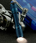 Quark LED Flashlight Pocket EDC with Clip, High CRI Beam next to a fishing reel and tackle box, tactical light for everyday carry.