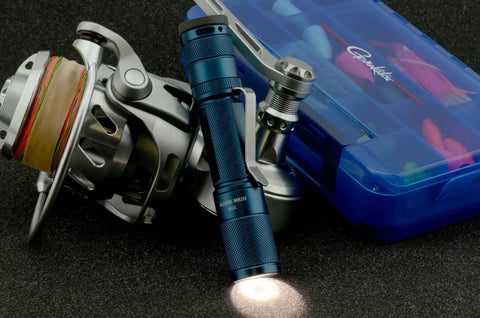 Quark LED Flashlight Pocket EDC with Clip, High CRI Beam next to a fishing reel and tackle box, tactical light for everyday carry.