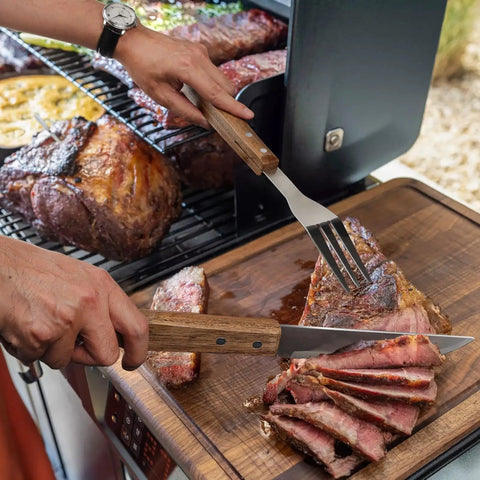 Slicing meat with a Stainless Steel BBQ Grill Tools Set With Ergonomic Wood Handles Includes Spatula Tongs Knife Fork And Carry Bag.
