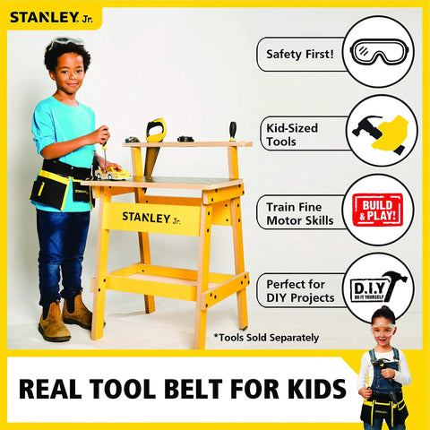 Child wearing Junior Tool Belt Set for Kids Ages 5 and Up with Realistic Play Tools, standing beside a yellow tool bench.