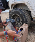 Person setting up portable propane water heater with constant temperature control for camping showers near an off-road vehicle.