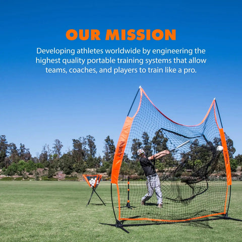 Baseball player using orange and black portable training net on a field under blue sky, surrounded by trees.