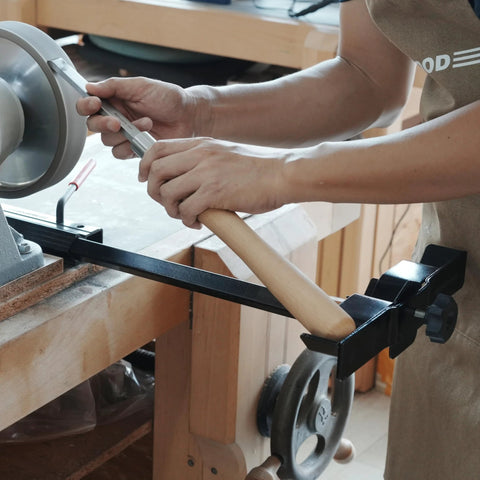BG-GRIND4 4-piece woodworking sharpening jig in use, clamped to a bench grinder while sharpening a chisel.