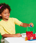 Child playing with Travel Magnetic Construction Set With 26 MicroMAGS Tiles, building colorful block structure on a table.