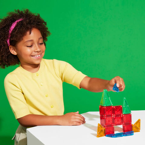 Child playing with Travel Magnetic Construction Set With 26 MicroMAGS Tiles, building colorful block structure on a table.