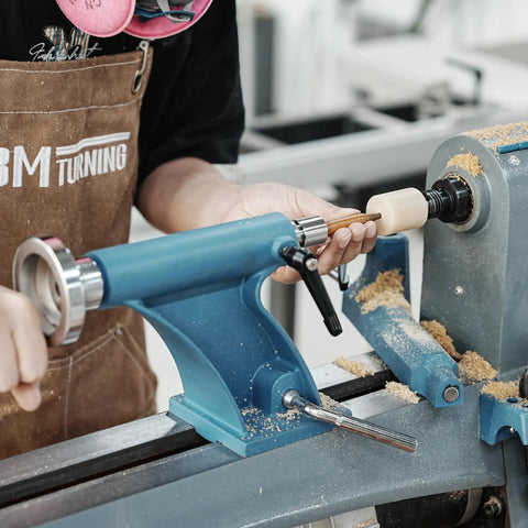 Person using Pen Press Kit for Woodturning Lathes with 2MT Taper, assembling pen on lathe, visible blue press and wood shavings