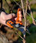Hand holding PX Medium Pruner For Precision Slicing With Number Two Blade Ergonomic Garden Shears pruning small branch.