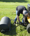 Man attaching Spyker 300lb Push Tow Commercial Lawn Roller With No Tools Handle to a lawn tractor on grass