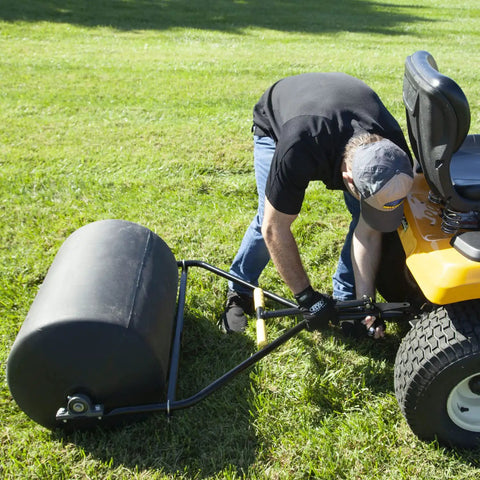 Man attaching Spyker 300lb Push Tow Commercial Lawn Roller With No Tools Handle to a lawn tractor on grass