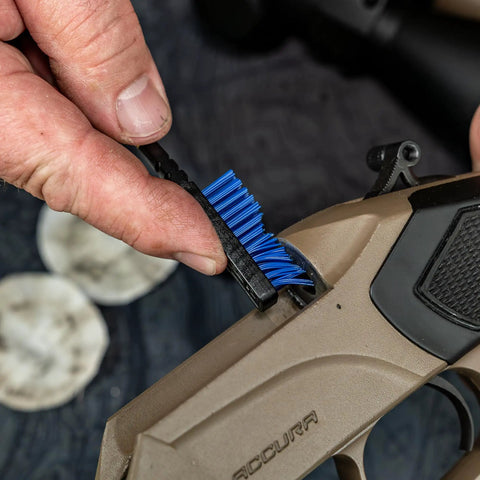 Using Caliber 50 Muzzleloader Cleaning Kit With Caliber Specific Bronze Bore Brush Pierce Point Jag Slotted Tip 100 Percent Cotton Patches Nylon All Purpose Cleaning Brush Straight Pick And Hand Tool Go To Gear For Your Muzzleloader Maintenance, a hand holds a blue nylon brush cleaning a muzzleloader breech.