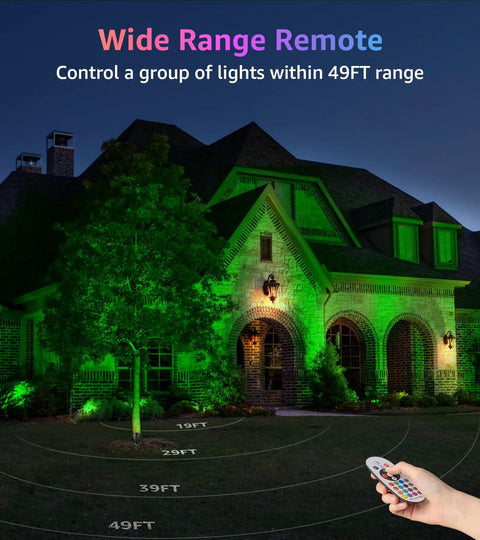 Wide view of a house lit with the Two Pack Outdoor RGBW LED Spotlight Kit With Remote Control, showing green lighting and remote in hand.