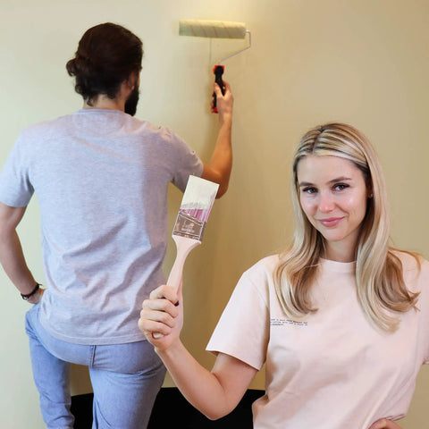 Woman holding brush and man using roller from Eight Piece Painting Roller Kit With Tray And Brushes for home DIY project.