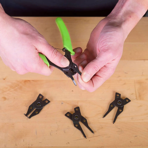 Person using 4 In 1 Snap Ring Pliers Set For Internal And External Rings, with interchangeable jaws, on wooden surface