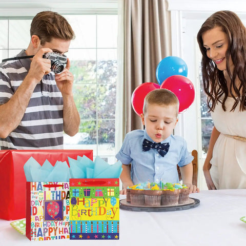 Two Pack 12.6 Inch Large Happy Birthday Gift Bags With Tissue Paper next to a boy blowing out candles at a birthday party