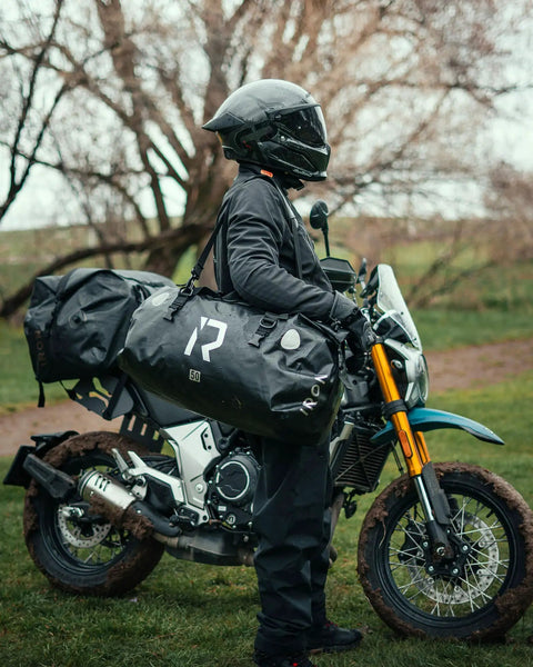Motorcyclist with Waterproof Motorcycle Dry Bag 30L Duffle Tail Bag N Saddle Bags on rugged ride, showing helmet and muddy motorcycle