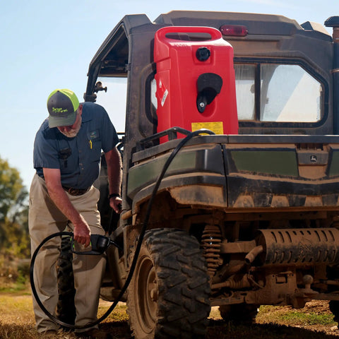 Person using Duramax Flo N Go 14 Gallon Gas Caddy On Wheels With 10 Foot Hose And Portable Fuel Tank Transfer Pump For Lawn Mowers Farm Marine And Home Use Gasoline Only Red 2024 Version in a rural setting