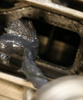Close-up of non metallic anti seize lubricant being applied to engine threads, visible dark gray paste for thread lubrication.