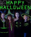 Group of children in Halloween costumes with glow in dark outfits under 'Happy Halloween' sign, showcasing spooky decor.