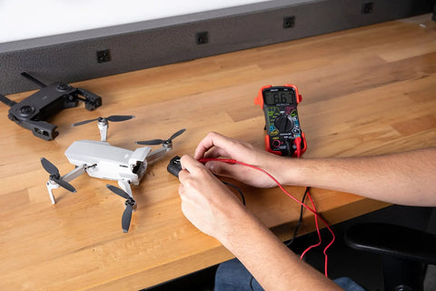 Person using Auto-Ranging Digital Multimeter For Automotive And Home Electrical Troubleshooting UL Certified on drone battery.