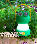 Green frog-shaped LED lantern surrounded by flowers, resembling Owl Themed Kid Friendly LED Lantern And Headlamp Set for camping.