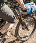 Cyclist with TetraRack M1 Fork Mount Rack For Bikes on MTB, carrying blue gear, QuickTrack Compatible, on dirt trail.
