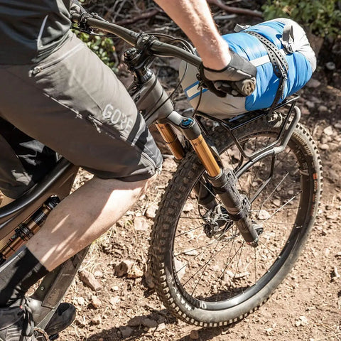 Cyclist with TetraRack M1 Fork Mount Rack For Bikes on MTB, carrying blue gear, QuickTrack Compatible, on dirt trail.