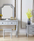 Elegant gray vanity set with mirror, stool, and drawers with decorative accents, set against a white wall.