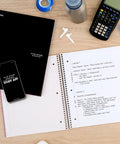 Hustle Ready Black Spiral Notebook With Five Subject Sections And College Ruled Paper Providing Clean Lines And No Bleed Pages Built For Daily Study Grinds And Phone Pairing on a desk with a smartphone and calculator.