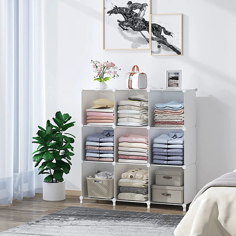 9 Cube White Storage Organizer Set in a living room, holding folded clothes and decor, near a plant and artwork on the wall