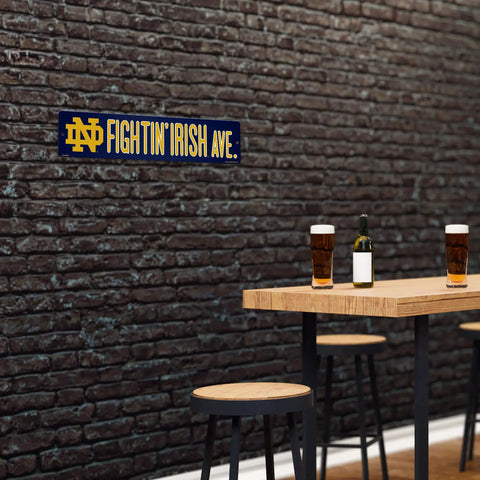 Notre Dame Fighting Irish 16 Inch Plastic Street Sign Wall Decor on brick wall with beer and stools, perfect for tailgating.