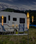 Outdoor scene with lit bamboo tabletop torches near a camper, featuring 16 Ounce Torch Replacement Canisters for Refillable Bamboo Torch Fuel Citronella Tabletop Torches Outdoor Patio Garden Decor Black No Fuss Easy Pour Wide Mouth Design with Snuff Cap for Safe Extinguishing.